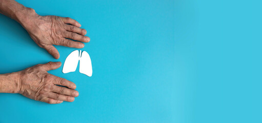 hands of an elderly person cut out of paper in the form of an organ lungs on a blue background, banner, copyspace. lung health in old age, be healthy concept