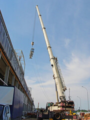 Fototapeta premium The boom of the truck crane lifts the equipment of the air conditioning system to the roof of the warehouse