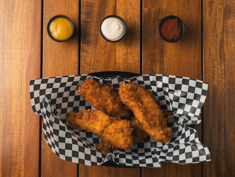 Plano cenital de tiras de pollo fritas y tres salsas de comida r&aacute;pida