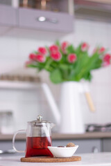 a glass teapot with tea and dessert stands on a white kitchen table against the background of a kitchen interior Vertical frame