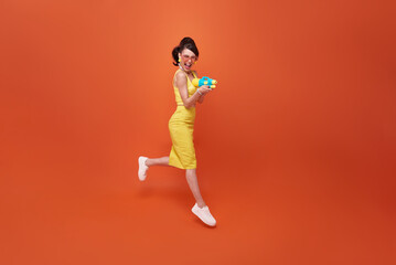 Jumping tourist woman traveling with water gun during Songkran festival studio on copy space orange background.
