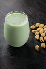 Organic pistachio milk in glass and pistachios on a dark green background. Non dairy alternative milk. Copy space