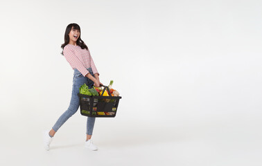 Happy Asian woman holding shopping basket full of vegetables and groceries, studio shot isolated on...