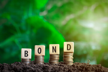 bond on a wooden block placed on a coin  with green bokeh nature background in investment bond concept  Raising Funds to Fund the Green Bond Program - obrazy, fototapety, plakaty