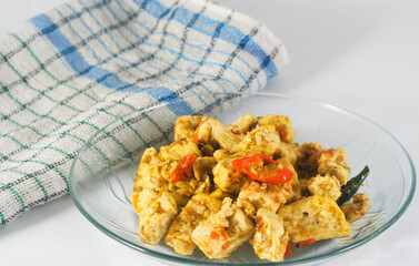 sliced tofu cooked dry with chilies served on a small plate with a napkin isolated on a white background