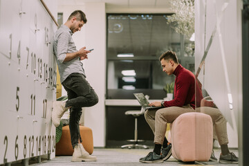 Two tired good looking male coworkers checking their social medias at the end of the working shift