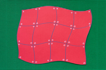 red paper shape with grid pattern on corrugated green paper background