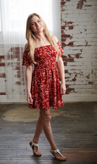 Beautiful blonde woman in red sundress roses for photo in loft - spring fashion