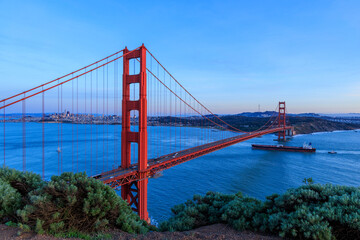 Fototapeta na wymiar Cargo ship sails into San Francisco Bay under Golden Gate Bridge at sunset