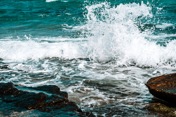 The wave breaks on the rocks, forming white foam. Tropical island, travel and vacation concept