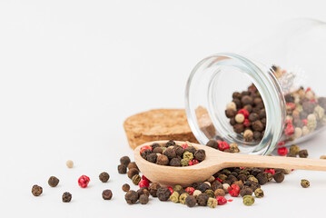 Close up of a mixture of peppercorns in wooden spoon  and glass jar scattered on a white background