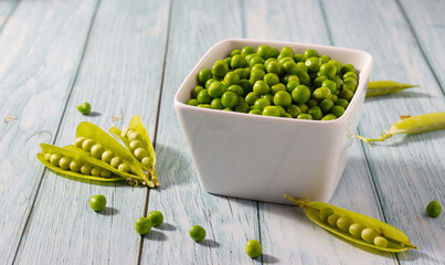 Close-up of organic peas in a white bowl on white wooden background. Concept of veganism, vegetarian and healthy food.
