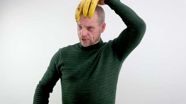 comic photo of man holding three spoiled bananas on his head as a hairstyle squinted eyes squint redhead with a gray beard and mustache green sweater white background make faces make faces