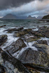 Fototapeta na wymiar Rough tide crashing onto rocks on the shoreline of Elgol with moody clouds in sky. Isle of Skye, Scotland, UK.