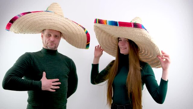 man and woman on white background in Mexican sombrero hats huge hat dressed like Napoleon he points finger as if is offering a trip warm sweaters waiting for warmth of the sea for relaxation