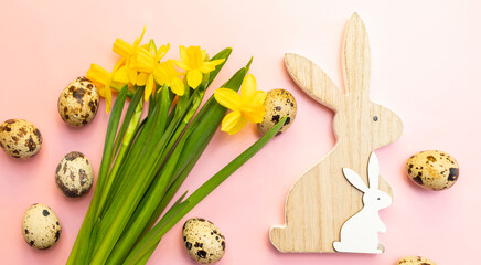 Wooden rabbit and bunny, yellow fresh narcissus flowers with green leaves, quail eggs on pink background. Easter poster,celebration.Flat lay greetings and present for Easter Day, horizontal plane - obrazy, fototapety, plakaty