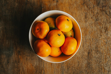 Photograph of white bowl with tangerines on a wooden background. Food concept