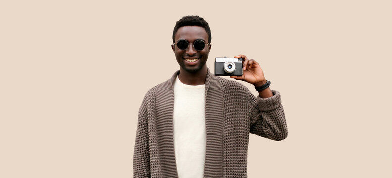 Portrait of stylish modern happy smiling young african man photographer with film camera taking picture isolated on gray background