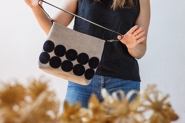 A woman shows a linen bag. Crossbody bag is made of linen and decorated with knitted black  decor.