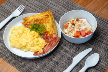 Kids menu, scrambled eggs, bacon, toast and muesli with yoghurt served on the restaurant table with plastic kids friendly eating utensil.