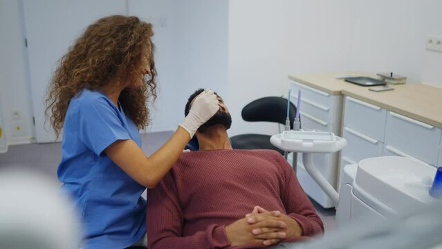 Young woman dentist doing doing preventive examination to multiracial man.
