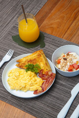 Kids menu, scrambled eggs, bacon, toast and muesli with yoghurt and a glass of orange juice served on the restaurant table with plastic kids friendly eating utensil.