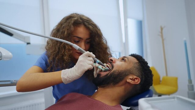 Young woman dentist doing doing preventive examination to multiracial man.