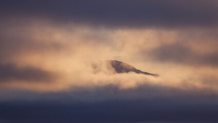 atardecer paisaje nevado, colina en invierno, con bruma y nubes bajas, picos de montañas rodeadas de nubes 