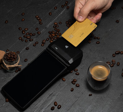 Paying contactless for an espresso at a smart POS with gold credit card. Coffee beans are the best morning energy. Cashless is the future.