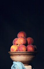 Red-yellow peaches on clay bowl on a rustic wooden table against dark background