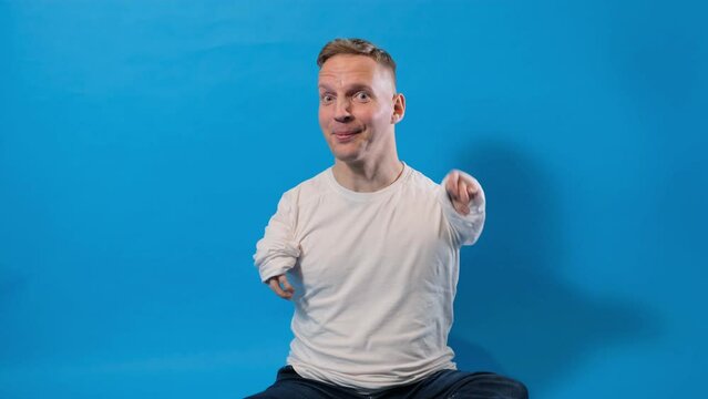a young man with disabilities smiles, waves amiably at the camera, greets someone, greets someone, stands on a blue background.