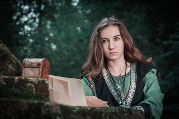 Young beautiful woman wearing man’s medieval style dress with old paper