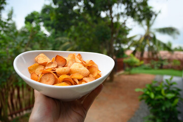 Organic Cassava chips in bowl in hand against tropical landscape. Indonesia popular hot spicy...
