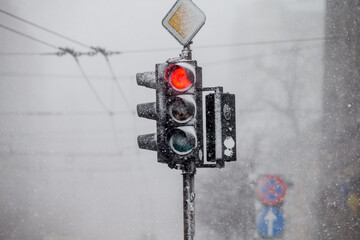 Red traffic light covered in heavy snow, during snow fall in city. Riga, Latvia