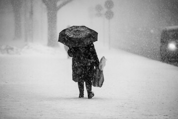Woman walking in heavy snow storm with an umbrella and winter coat. Riga, Latvia
