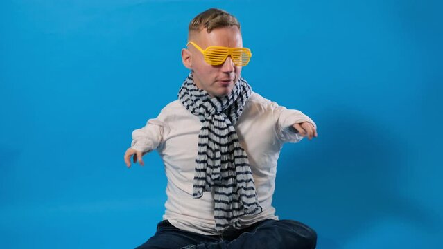 a man with disabilities in yellow stylish glasses is dancing merrily, fooling around on a blue background.