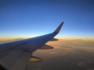 Naklejka na ściany i meble Photography of the plane's wing through the window, beautiful evening in the air