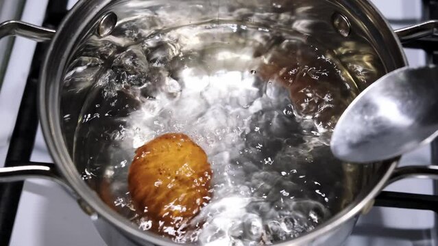 A person puts eggs in a pot of boiling water. Cooking of brown chicken eggs. Metal saucepan on a gas stove. Healthy eating. A dietary product. Close-up. Fast breakfast food. Slow motion 4K footage.