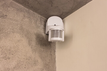 Motion detector or alarm detector for wall mounting, white, on a gray wall, in the corner