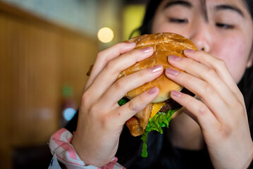 Young asian girl holding bacon cheese hamburger