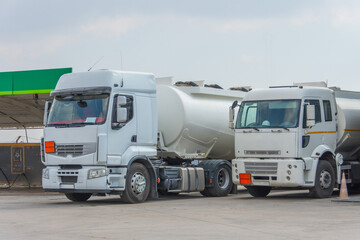 Fototapeta na wymiar Two fuel trucks delivering fuel to the city fuel station parking.