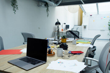 Office in use without people. Office desk cluttered with laptop and work supplies. Meeting room with no staff. Empty room for employee rest. Entrepreneurial business conference room.