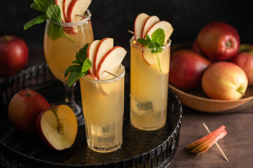 Three glasses of refreshing apple cocktail drinks with fresh red apples, dark background