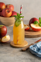 Apple juice in glass bottle, with fresh mint and red apples, wooden background.