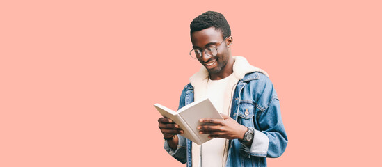 Portrait of smiling young african man student with book wearing eyeglasses isolated on pink background