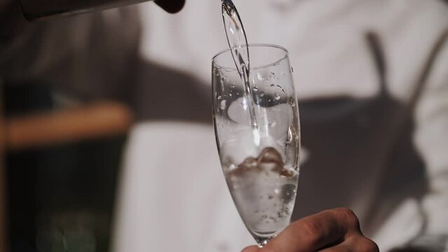Bartender pours cocktails into glasses. Bar in the open space.