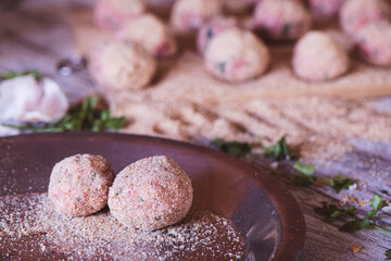 Two Raw meatballs in a plate and more in the background, on a kitchen table