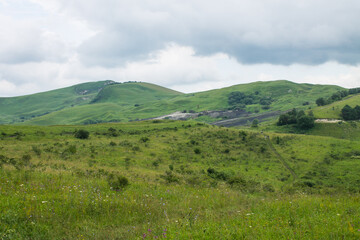 Fototapeta na wymiar Beautiful hilly landscape - small saddle mountain with green grass and trees on a cloudy summer day and space to copy