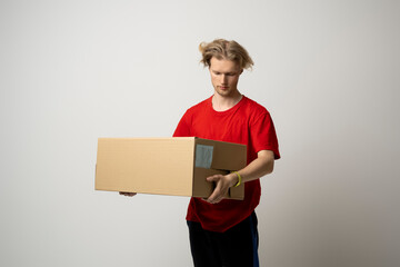 Delivery man in red uniform carry cardboard box in hands on white background. Delivery guy give parcel shipment.