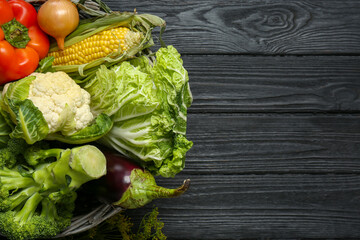 Different fresh vegetables in wicker basket on black wooden table, top view with space for text. Farmer harvesting